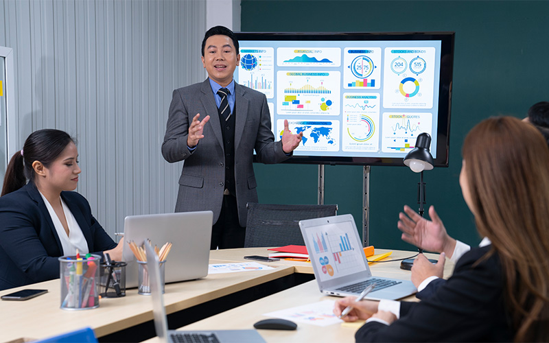 Businessman presenting investor financial data and global reports on screen.