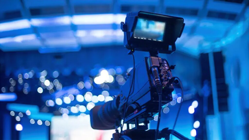 Professional video camera on tripod in a blue-lit studio with blurred bokeh lights in the background