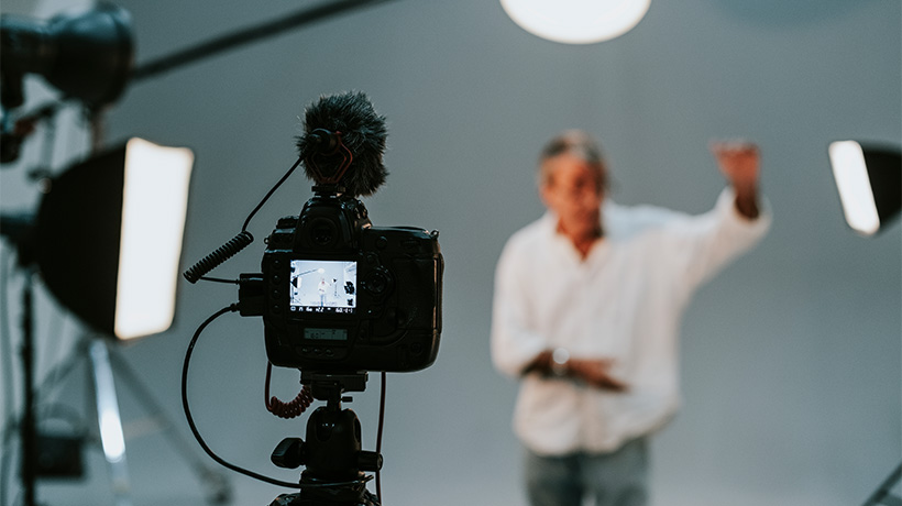 DSLR camera records person in studio with lights and backdrop.