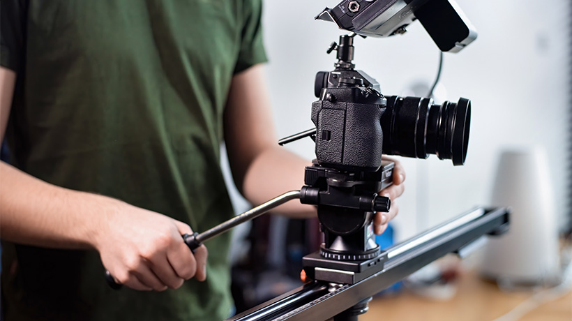 Person adjusting camera on slider rail for smooth video production shots.